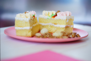 Split biscuit cake with protein cream and nuts in a plate on a white, pink and silver background. Shallow depth of field.
