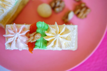Rectangular biscuit cake with protein cream and nuts in a plate on a pink background. View from above. Shallow depth of field
