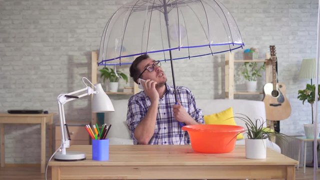 Man under an umbrella on the phone reports about the flood in his apartment