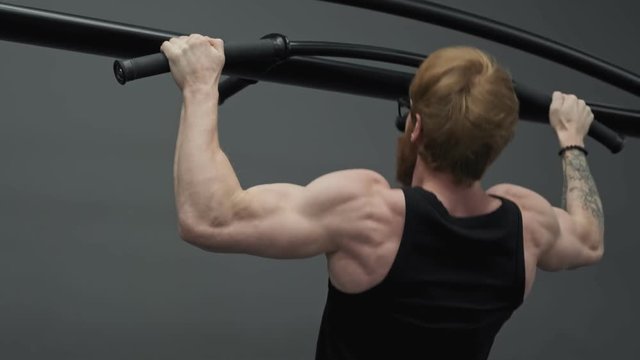 Close up man exercising and doing pull ups in gym from back. Redhead man doing pull-ups on bars