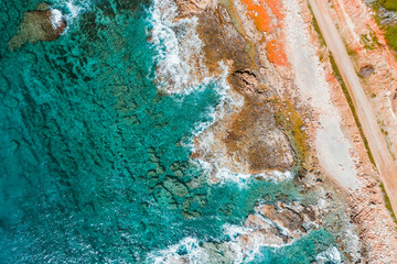 Overhead view of turquoise sea, waves and a rocky shoreline