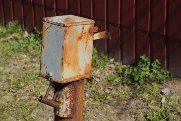 old gray brown rusty metal box for electricity on a pole outside the fence