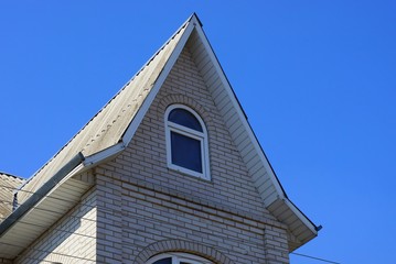 Obraz premium gray brick attic of a private house with a window against the blue sky