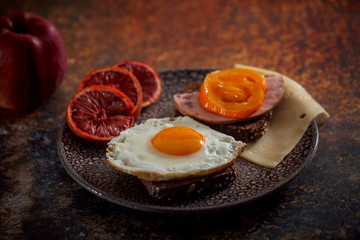 Grain bread with fried egg, tomato, cheese and bacon on ceramic plate with red orange 