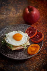 Grain bread with fried egg, tomato, cheese and bacon on ceramic plate with red orange 