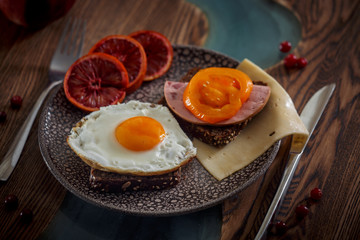 Grain bread with fried egg, tomato, cheese and bacon on ceramic plate with red orange 
