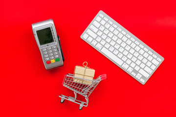 buying products with card machine, keyboard and mini trolley on red background top view