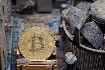 Dirty golden bitcoin inside an old broken computer covered with dust