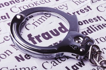 Handcuffs frame the word fraud among newspaper cuttings