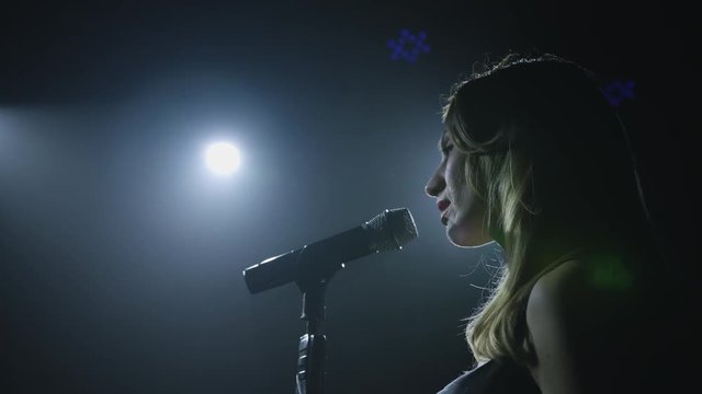 Close-up of the face of the singer with microphone on a black smoky background. The singer sings a song on stage in the dark, smoke, purple light, concert 4k