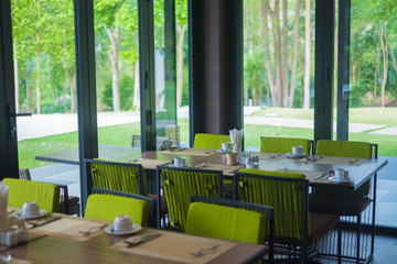 Empty restaurant part of hotel with table and armchair near windows and garden view.