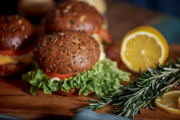 Obraz na płótnie Canvas Dark burger with grain bread on dark ceramic plate, salad, rosemary and lemon