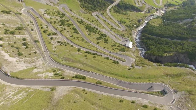 DRONE: Cars cruising along a mountain switchback road, tourists enjoying the stunning green landscape. Soft spring sun illuminates breathtaking meadows, hills and valleys of the Italian Dolomites.