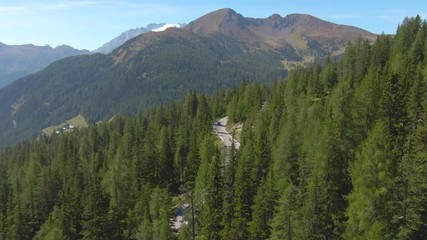 DRONE: Two car drivers enjoying a carefree drive on a spring afternoon, taking in tue stunning green landscape of Italian Dolomites. Beautiful aerial view of snow covered mountain tops in the distance