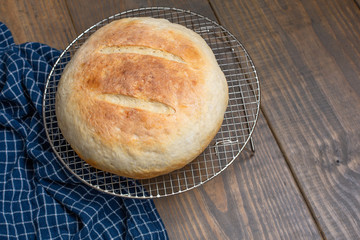 Round Loaf of Freshly Baked Sourdough Bread on Cooling Rack on Wood Table with Blue Kitchen Towel