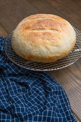 Round Loaf of Freshly Baked Sourdough Bread on Cooling Rack on Wood Table with Blue Kitchen Towel