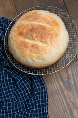 Round Loaf of Freshly Baked Sourdough Bread on Cooling Rack on Wood Table with Blue Kitchen Towel
