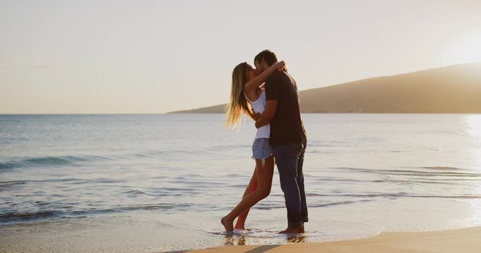 Young attractive couple embracing and kissing on the beach at sunset in slow motion, summer romance