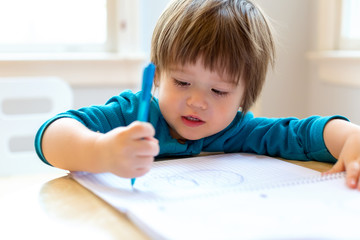 Naklejka premium Toddler boy drawing with pen and paper at his desk