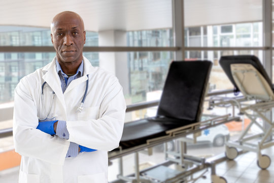 African Doctor Standing At Corridor In Front Of Bed At Hospital With Larges Window Background , Crossed Arms,