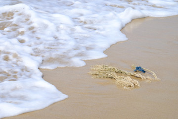 Piece of tendering rope on the sand beach with beautiful bubble foam of sea wave