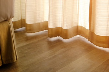 Closeup wood floor at the corner of a bed in bedroom with beautiful sunlight through yellow bottom...