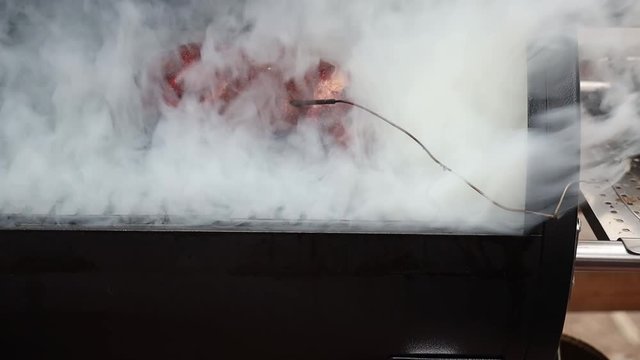 Heavy smoke from a pellet grill obscures the pork on the grate, the smoke briefly clears to give a view of the pork butt.