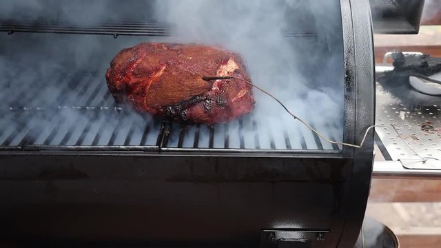 Opening the lid of a smoker to reveal heavy smoke and a pork butt before closing the lid again.