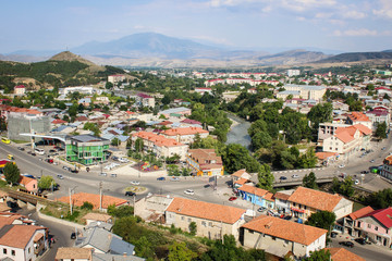 Fototapeta na wymiar View of the city of Akhaltsikhe, in Georgia. A small town, orange, red roofs, low-rise houses, a river, mountains, a highway, cars.