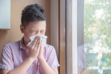 Sick asian boy blowing nose into tissue, Unhealthy child suffering from running nose or sneezing...