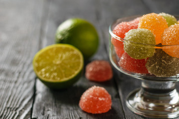 Colorful marmalade in a glass bowl and lime on a black wooden table.