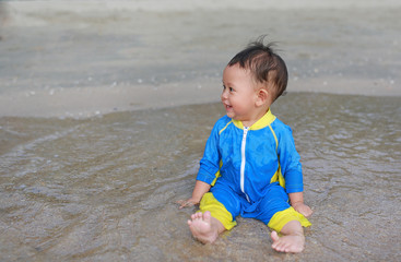 Portrait of Asian baby boy in swimming suit sitting on the sand beach.