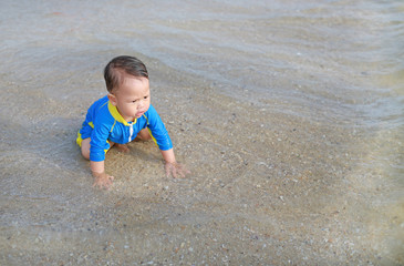 Portrait of Asian baby boy in swimming suit sitting on the beach.