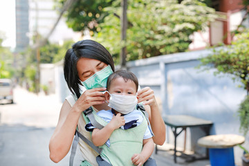 Asian mother carrying her infant baby by hipseat outdoor with wearing a protection mask against PM...