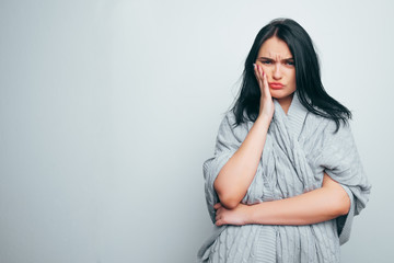 A beautiful brunette girl holds her hand over a sore spot. Teeth pain, illness, sad.