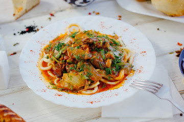 Uyghur lagman with fresh meat and vegetables on white plate.