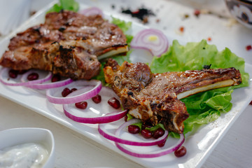 Barbecue ribs on white plate, meat dish served with onion and herbs.