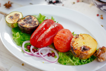 Grilled vegetables -  potato, tomato, bell pepper, eggplant and zuccini on skewer over a white plate.