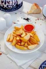 Fried potatoes with red tomato sauce on the white plate.