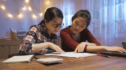Young asian family having debt problems not able to pay out loan. Female in glasses and sister studying paper from bank while managing domestic budget together in kitchen interior. girls accounting