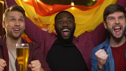 Sports fans with Spanish flag cheering for national team, watching game in pub - Powered by Adobe