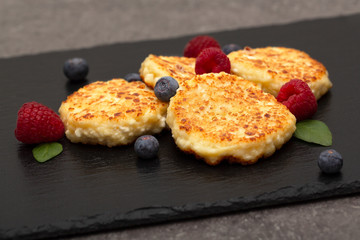 Cheesecakes from cottage cheese. Cottage cheese pancakes or curd fritters decorated fresh raspberries and blueberries. Healthy and diet breakfast. 