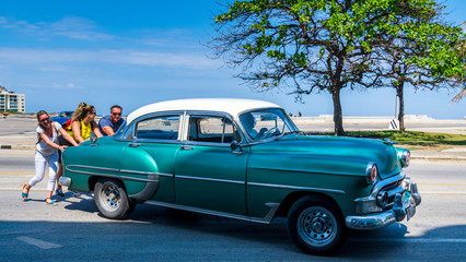 Cuba, Havana: Old American classic car cab, broke down, tourists are pushing the car away from the street. Just a hilarious moment.