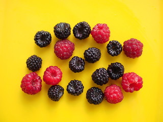 Berries of red and black raspberry on a yellow background