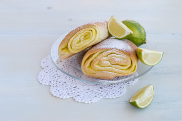 Sweet dessert. Fresh homemade buns with fruit filling and a juicy tropical lime on a round plate on a light wooden table. Selective focus.