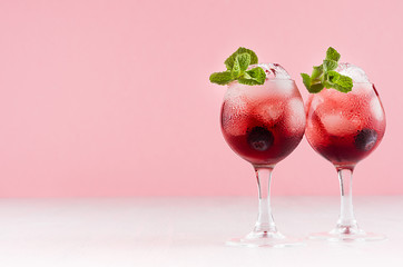 Elegant summer fresh red bright drinks with ice cubes, blueberry, green mint  on fashion pastel pink color background and white wood table.