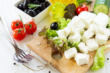 Ingredients for cooking qreek salad with fresh vegetables, feta cheese and black olives on wooden table.