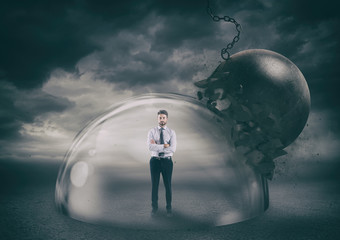 Businessman safely inside a shield dome during a storm that protects him from a wrecking ball....