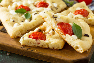 Traditional Italian Focaccia with rosemary, tomatoes and feta - close-up homemade flat bread focaccia.