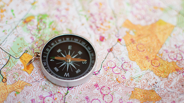 Round compass on colorful topographic map for orienteering or rogaining sport, close up view at shallow depth of field. Travel, recreation and active lifestyle concept.
